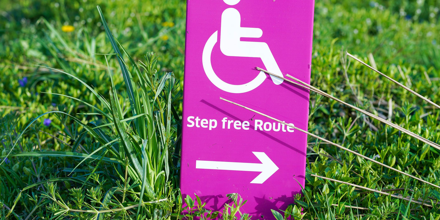 Bright pink sign in the grass with a wheelchair symbol and text that says "Step free route"