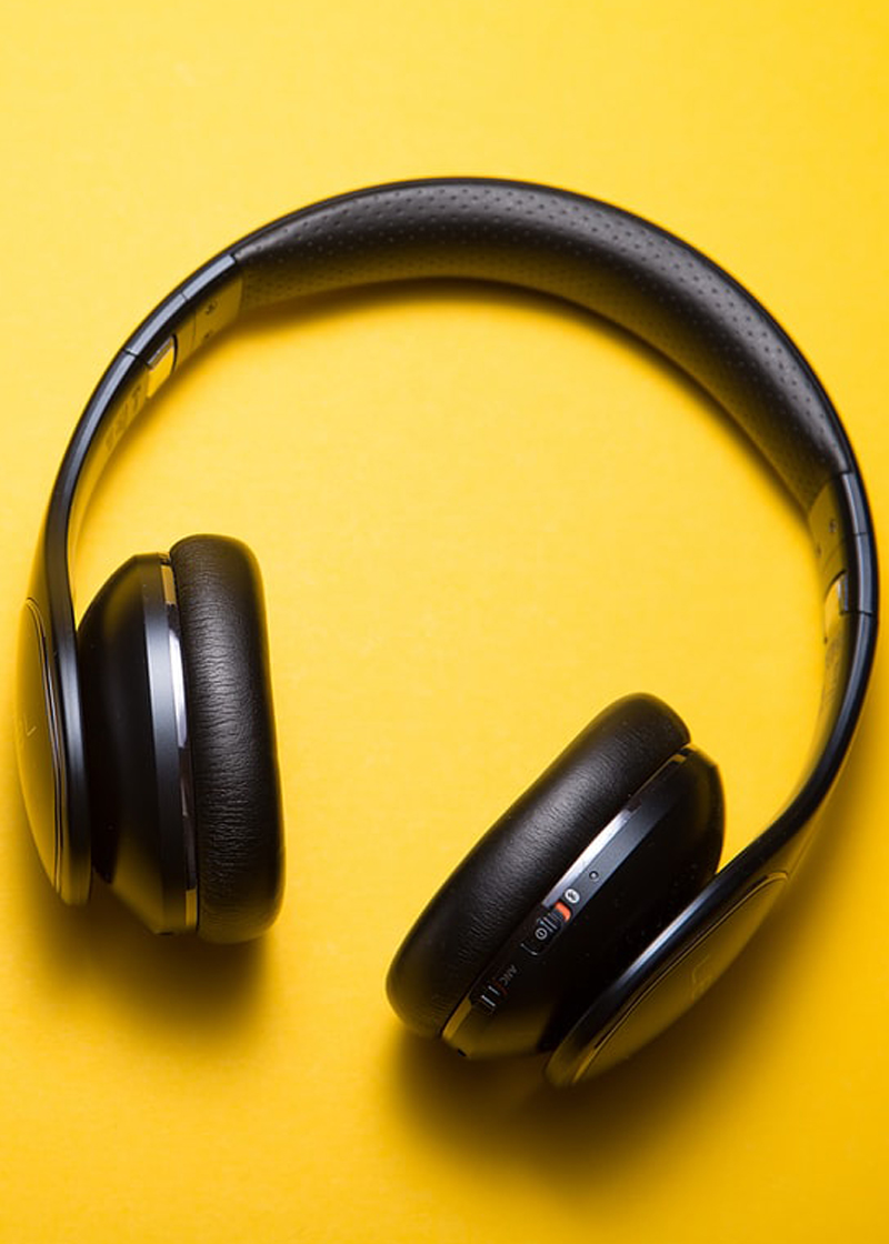 A pair of black headphones on a bright yellow background.