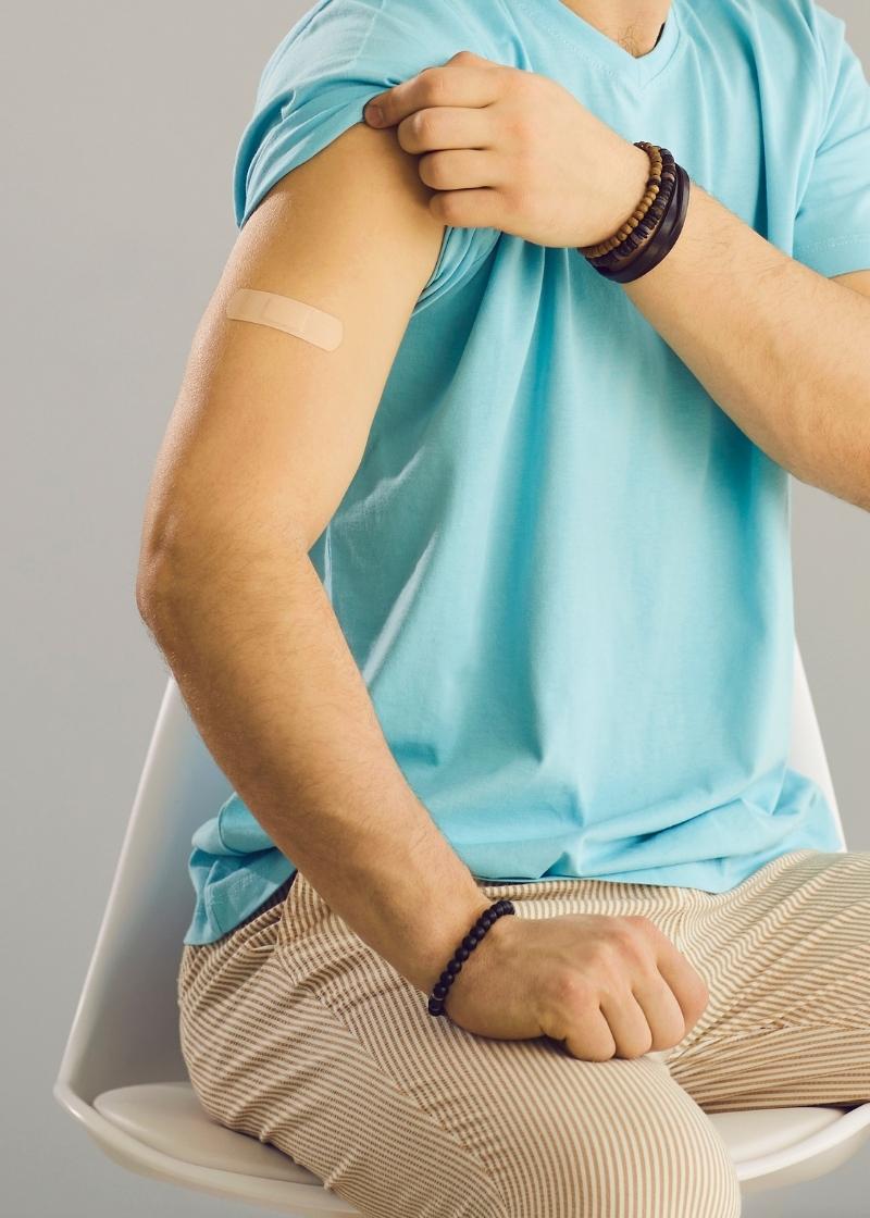 A person sitting on a chair rolling up their sleeve to show a band aid on their upper arm