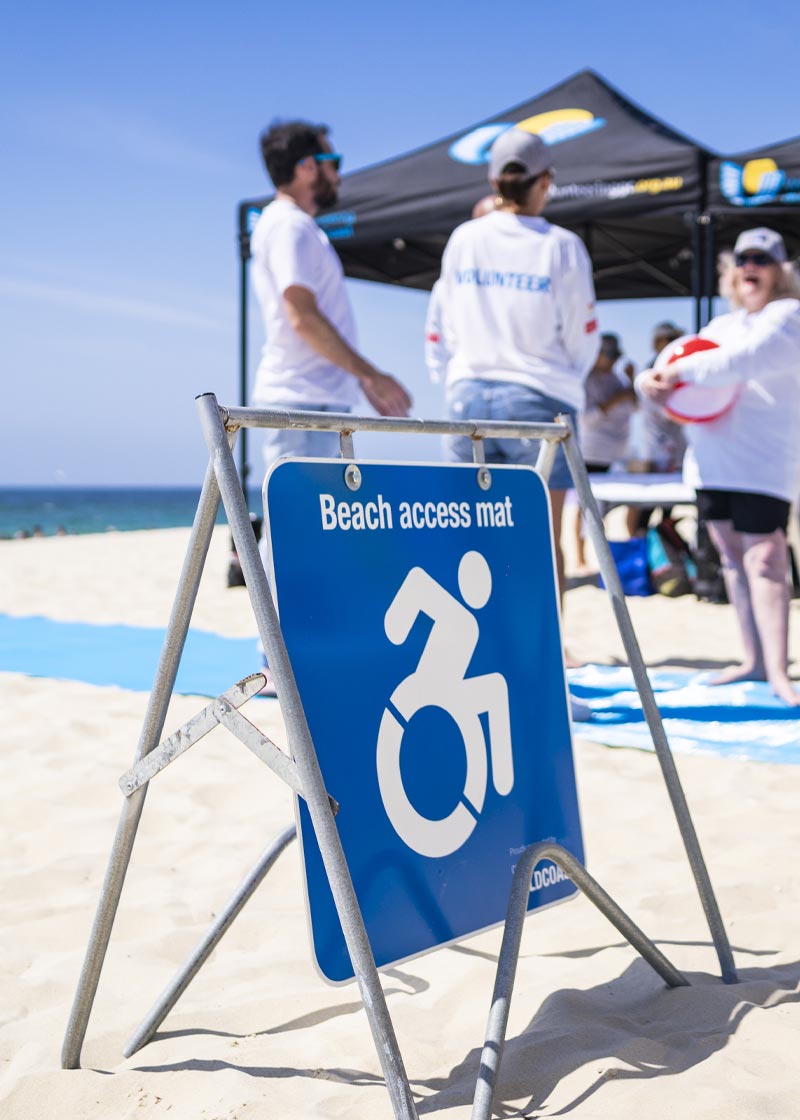Sign on the beach that says "Beach access mat" with the blue mat running behind it