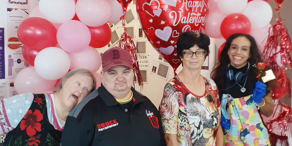 Four people standing with pink Valentine's Day balloons behind them