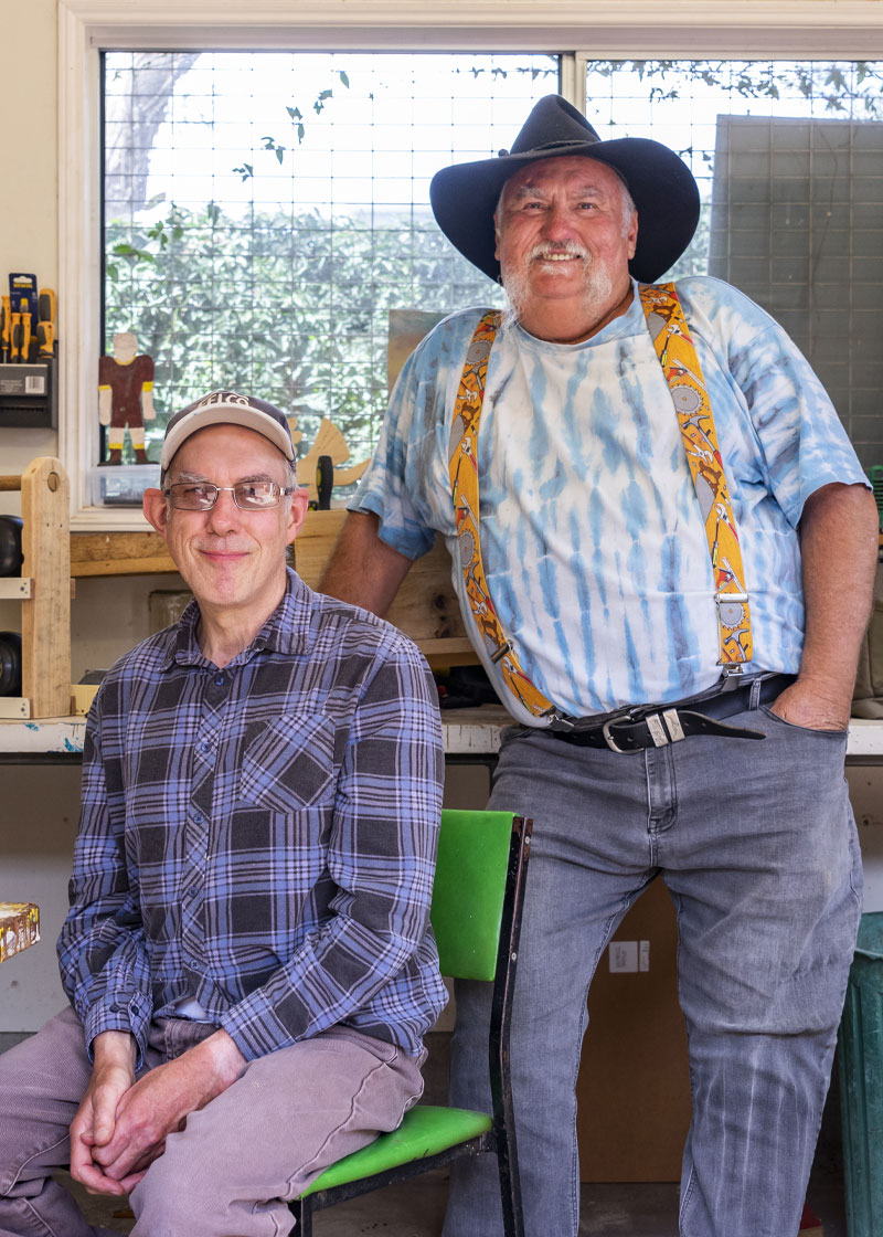 Two men in a shed. One is standing and one is sitting down.