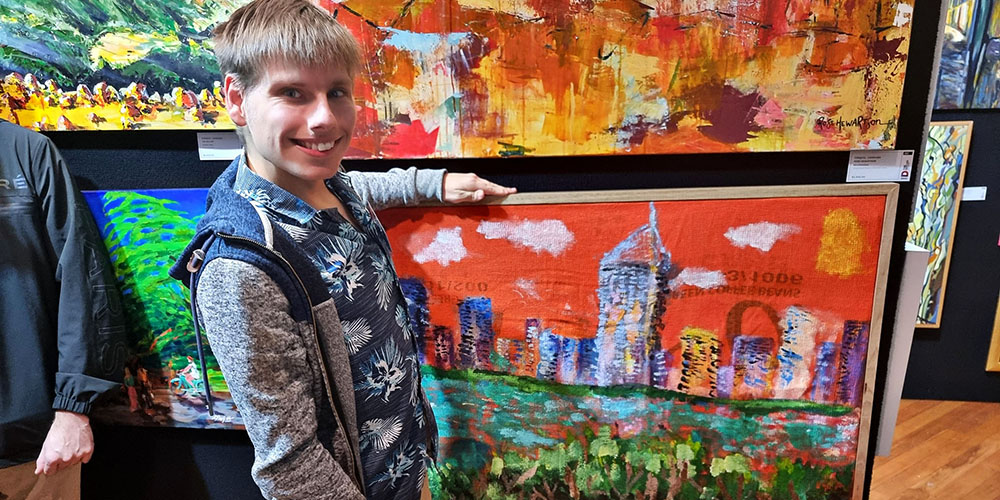 Liam standing beside his artwork City of Gold Coast, hung at the Doyles