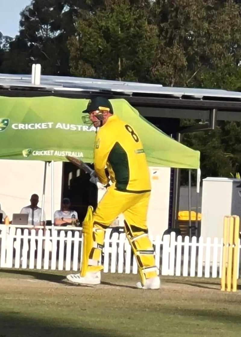 A men in a yellow and green cricket uniform stepping up to bat