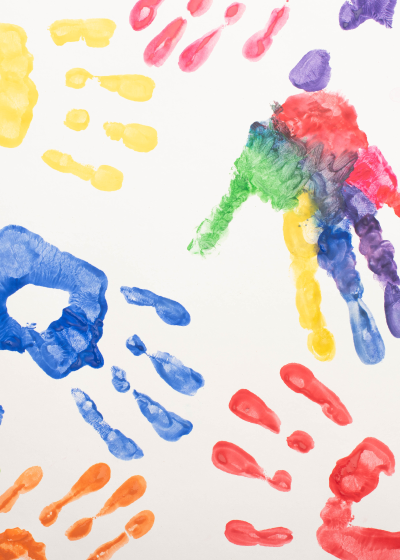 Various different hand prints are painted on a white piece of paper in different colours. One hand print is in a mix of colours. 