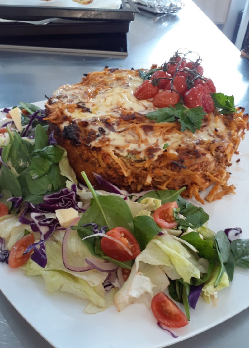 A close up image of a Ricotta and Spinach Stuffed Spaghetti Pie topped with melted cheese, mini tomatoes and a side of green salad