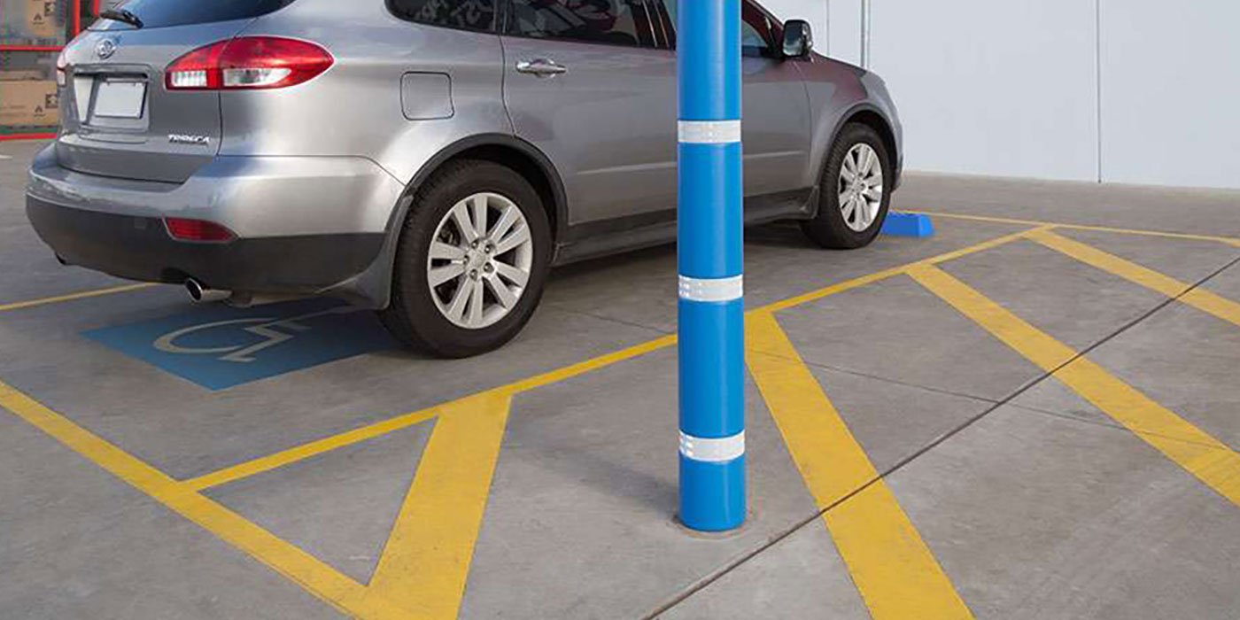 A picture of a silver car parked in an accessible car park. there is a blue bollard and yellow striped section beside the car.
