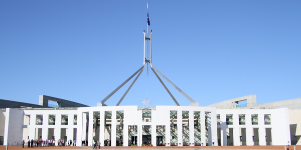 A photo of parliament house, with a blue sky in the background. The building is white and spans the length of the photo. 